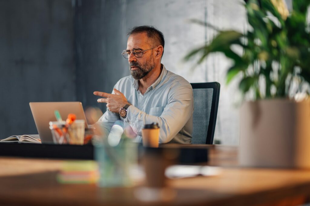 Mature businessman sitting at modern office and working on a laptop.